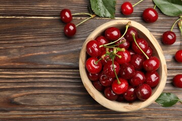 Fresh wet cherries in bowl and leaves on wooden table, flat lay. Space for text