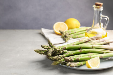 Fresh raw asparagus, oil and lemon on light grey table, closeup. Space for text