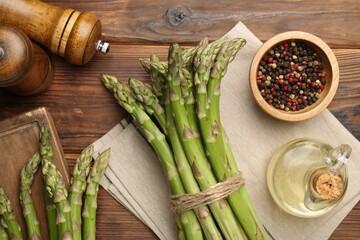Fresh raw asparagus, spices and oil on wooden table, flat lay