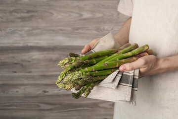 Woman holding fresh raw asparagus near wooden wall, closeup