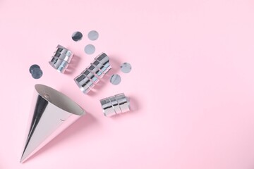 Shiny party streamers, confetti and cone on light pink background, top view. Space for text