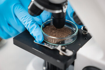 Scientist examining soil sample under microscope in laboratory, closeup