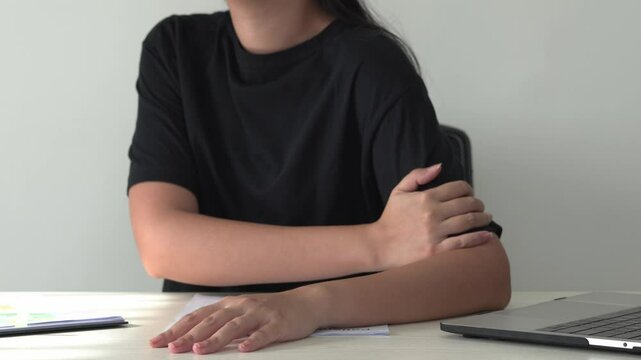 Young asian business woman is suffering pain on wrist, finger and arm, arthritis inflammation while working. Woman is massaging herself and doing exercise with her hands to relax and to relieve pain.