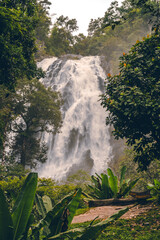 Obraz premium High-angle shot of a waterfall in the forest at Klong Lan National Park, Thailand. The water flows strongly from a cliff surrounded by trees and moss on rocks. Idea for a nature background.