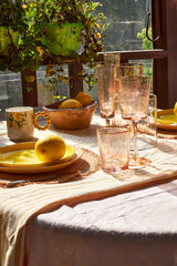A cozy summer table on a veranda with lemons, yellow tableware, and textured glassware. Warm sunlight creates a cheerful, rustic, and welcoming atmosphere for an outdoor meal