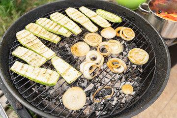 Vegetables cooking on a barbecue. Zucchini, carrots and onion. Smoke is rising. It looks really delicious. Outdoor concept.