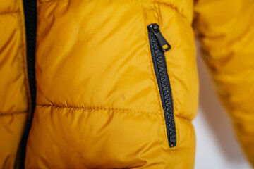 Detail of a mustard yellow puffer jacket with black zipper — winter wear concept. © Alena Vilgelm