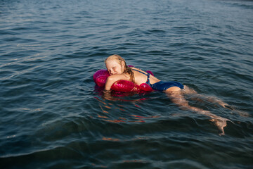 Child enjoying summer, floating face-down on a pink shell-shaped swim ring.