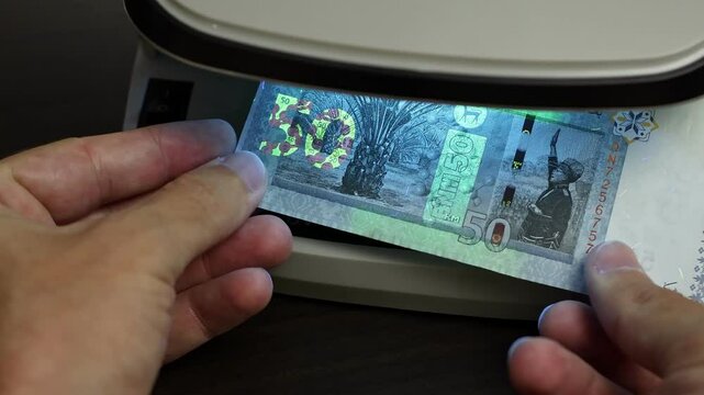 Examination of malaysian ringgit (MYR) cash money with UV counterfeit detector. Concept of authenticity check, fight against counterfeiting of banknotes, anti fraud measures in Malaysia. Close up view