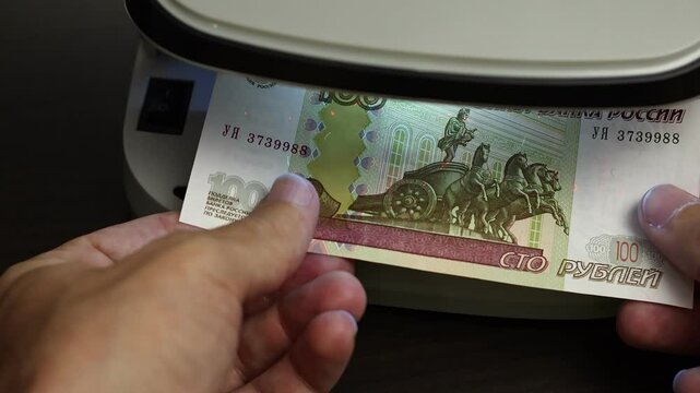 Examination of russian ruble (RUB) cash money with UV counterfeit detector. Concept of authenticity check, fight against counterfeiting of banknotes, anti fraud measures in Russia. Close up view.