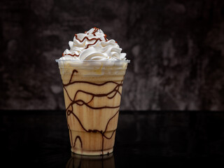 Vanilla milkshake with chocolate syrup in clear glass on dark background.