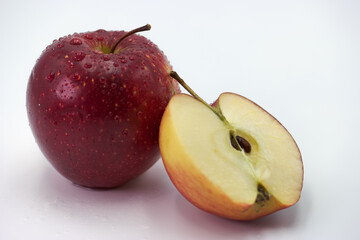 Fresh red apple and sliced half with droplets of water on a clean white background