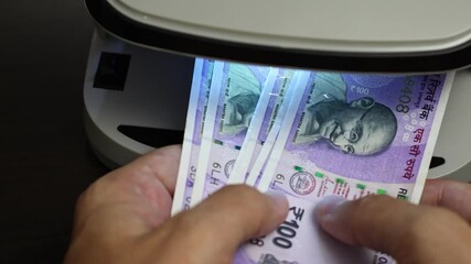 Examination of indian rupee (INR) cash money with UV counterfeit detector. Concept of authenticity check, fight against counterfeiting of banknotes, anti fraud measures in India. Close up view.