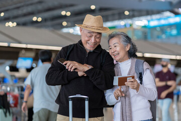 happy asian senior couple standing in the airport terminal,old woman holding passport and tickets,elderly man looking at a watch,waiting for boarding,airlines travel for summer vacation trip