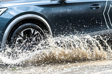 Close-up of car wheel splashing through flooded street during rain – urban weather hazard and...