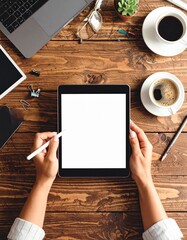 Overhead view of hands holding a tablet with a stylus, surrounded by office supplies on a wooden desk.