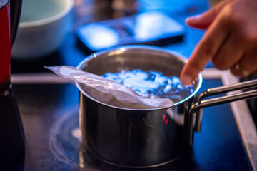 A candid kitchen scene showing a woman preparing rice, as boiling water steams from the pot — capturing the simplicity and warmth of home cooking.