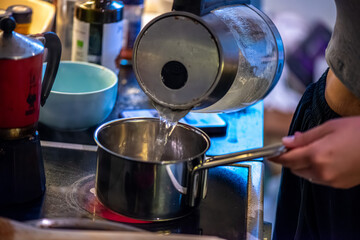 A candid kitchen scene showing a woman preparing rice, as boiling water steams from the pot —...