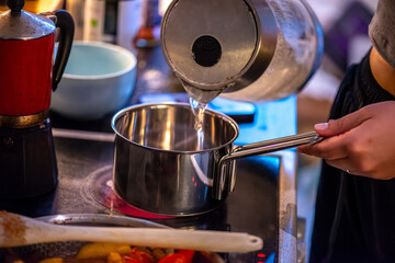 A candid kitchen scene showing a woman preparing rice, as boiling water steams from the pot — capturing the simplicity and warmth of home cooking.