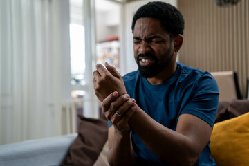 Black man suffering from wrist pain at home, painful grimace on face, indoor injury, health issue, physical discomfort