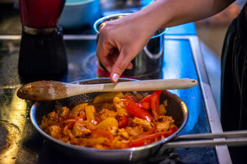 A close-up, high-detail macro shot capturing a woman preparing chicken sauté, showcasing sizzling ingredients, textures, and cooking action in a warm kitchen environment.