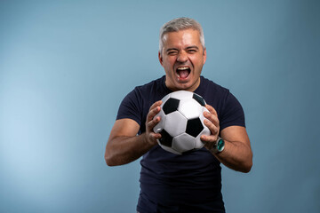Mature excited man holding soccer ball, looking at camera, happy and enthusiastic, victory feeling,...