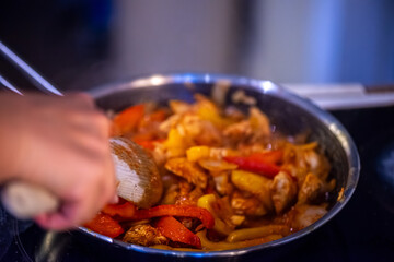 A close-up, high-detail macro shot capturing a woman preparing chicken sauté, showcasing sizzling ingredients, textures, and cooking action in a warm kitchen environment.