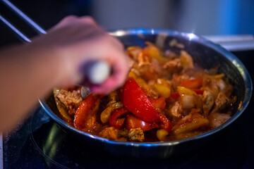 A close-up, high-detail macro shot capturing a woman preparing chicken sauté, showcasing sizzling ingredients, textures, and cooking action in a warm kitchen environment.