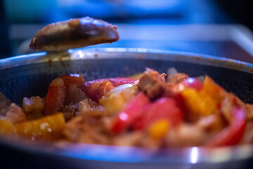 A close-up, high-detail macro shot capturing a woman preparing chicken sauté, showcasing sizzling ingredients, textures, and cooking action in a warm kitchen environment.
