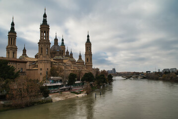 The image shows the Stone Bridge over the Ebro River in Zaragoza, Spain, with the Basilica of Our Lady of the Pillar in the background.