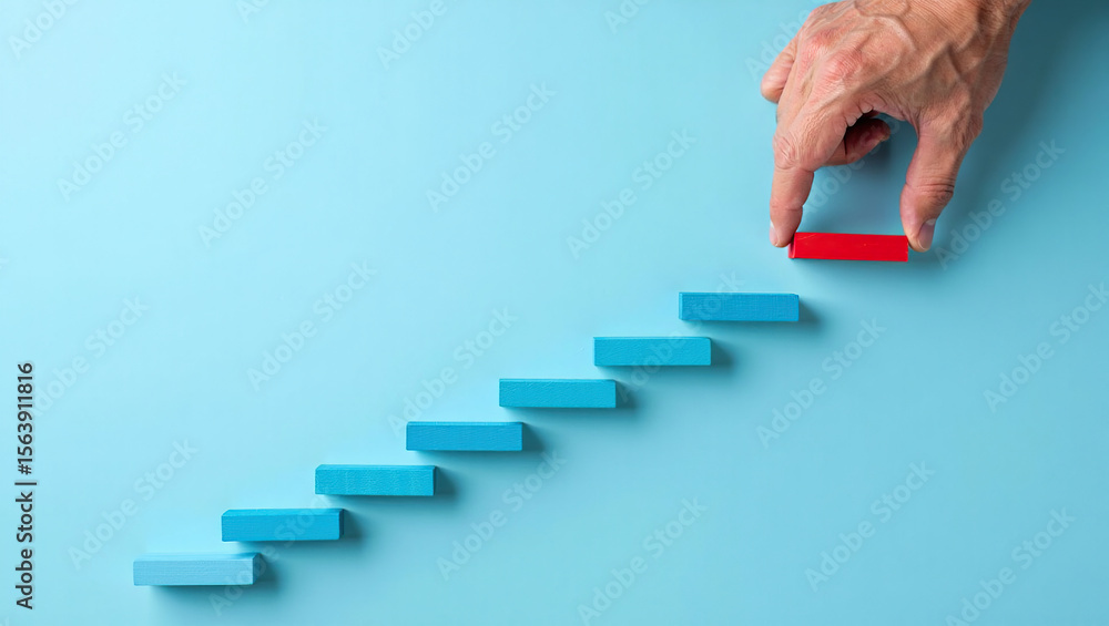 Poster hand placing red block on ascending staircase of blue blocks symbolizing step-by-step progress and a