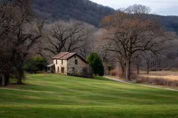 Obraz premium Rustic stone barn with weathered roof surrounded by bare trees and green fields image