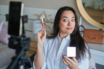 Young woman doing her makeup in front of the camera for her video blog. Social media. Life online.