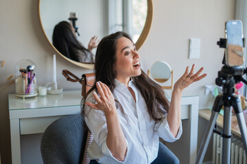 A young woman is filming a video on her phone for a blog in her room. Social media. Online life.