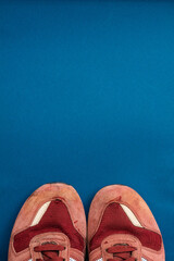 Top-down view of a pair of red sneakers placed on a blue background, showing visible wear and tear,...