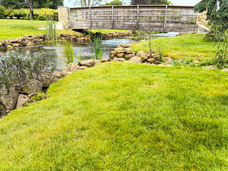 Wooden bridge over park stream surrounded by green grass and rocks