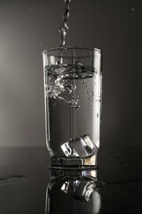 Fresh water splashing out of glass on mirror table against gray background