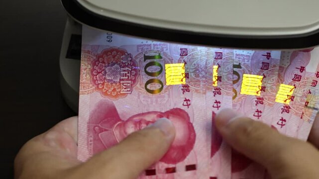 Examination of Chinese Yuan (CNY) cash money with UV counterfeit detector. Concept of authenticity check, fight against counterfeiting of banknotes, anti fraud measures in China. Close up view.