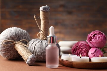 Massage bags, cosmetic product, burning candles and peony flowers on dark beige table, closeup. Spa...