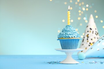Burning candle in cupcake, sprinkles and party hats on light blue table against turquoise...