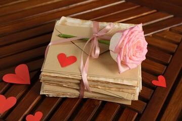 Stack of love letters, rose flower and paper hearts on wooden table indoors, above view