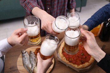 Friends clinking glasses of beer at wooden table, closeup