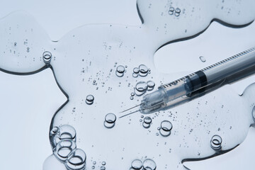 A syringe for injection in an appetizing drop with bubbles. Blue steel background.