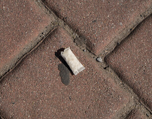 Used nicotine pouch discarded on a pavement tile. Close-up of urban litter and street pollution. Concept of waste, addiction, and public cleanliness