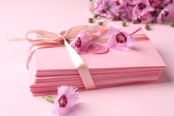 Stack of love letters and flowers on pink background, closeup