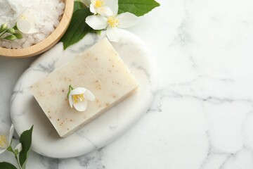 Soap bar, sea salt and jasmine flowers on white marble table, flat lay. Space for text