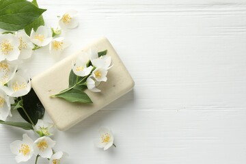 Soap bar and jasmine flowers on white wooden table, flat lay. Space for text