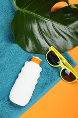 Beach towel, sunglasses, sunscreen and leaf on orange background, flat lay