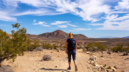 A person hiking on a desert trail under a vibrant blue sky dotted with wispy clouds - Powered by Adobe