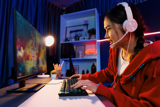 Host channel of young beautiful Asian gaming streamer playing fighting Moba at battle arena game on pc screen with multiplays, wearing pastel headphone at neon digital light modern room. Stratagem.